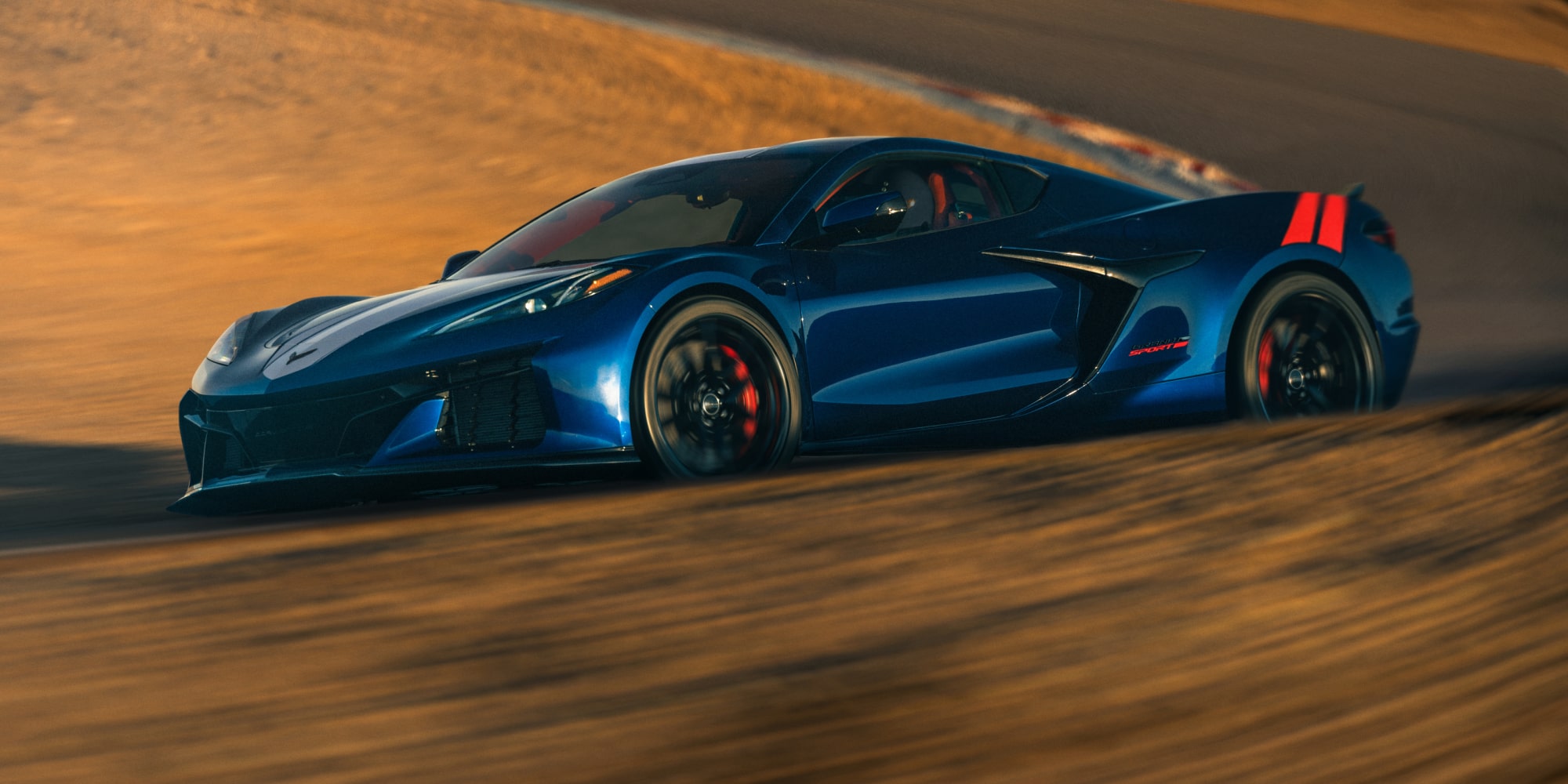 Une Chevrolet Corvette Grand Sport bleue 2027 file à toute vitesse dans un virage couvert de sable, avec de la poussière qui tourbillonne autour de la voiture dans une lumière dorée et chaleureuse.