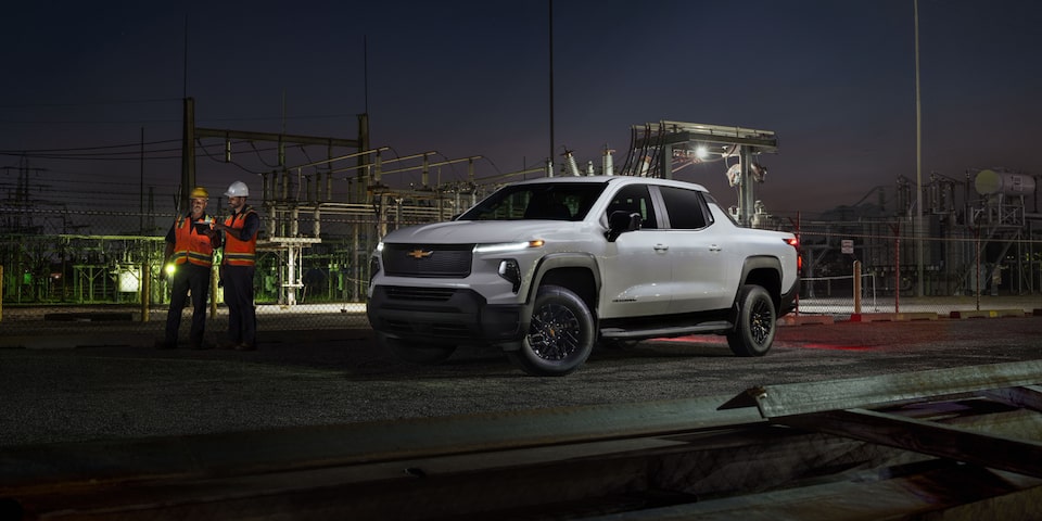 Vue latérale avant du camion de travail Chevrolet Silverado EV 2025 stationné au bord de la route la nuit.