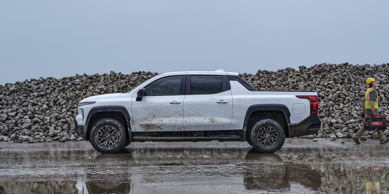 Vue latérale d’un camion de travail Chevrolet Silverado EV 2025 blanc stationné dans un chantier trempé.