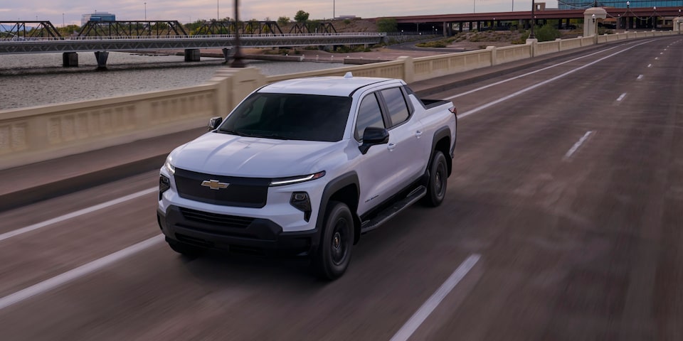 Vue latérale avant du camion de travail Chevrolet Silverado EV 2025 en mouvement sur la route le soir.
