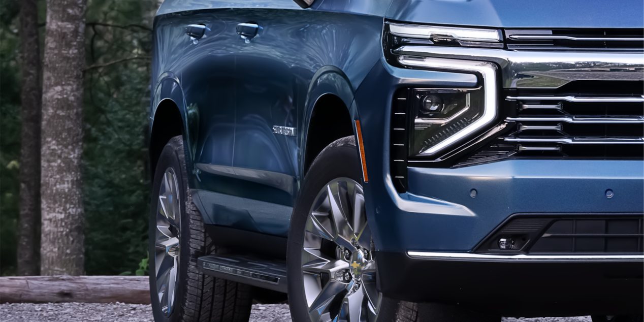 Close-up view of the 2025 Chevrolet Suburban's exterior passenger side parked near a wooded area.